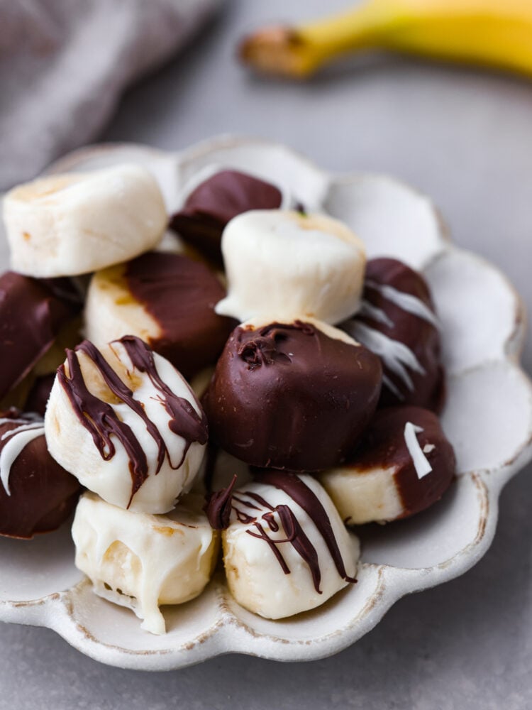 Prepare your tastebuds for these luscious chocolate covered bananas! With just a few simple ingredients, you'll be whipping up a creamy, chocolatey treat that's sure to bring a smile to your face. Chocolate dipped bananas served on a white scalloped dish.