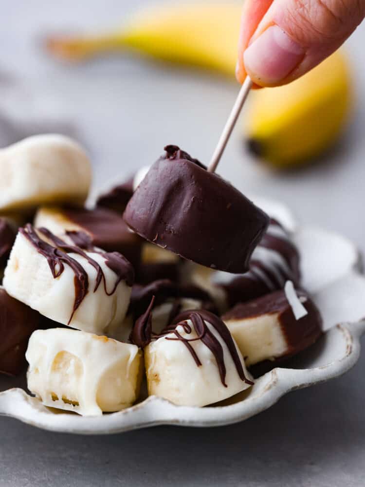 Prepare your tastebuds for these luscious chocolate covered bananas! With just a few simple ingredients, you'll be whipping up a creamy, chocolatey treat that's sure to bring a smile to your face. Picking up a chocolate covered banana with a toothpick.