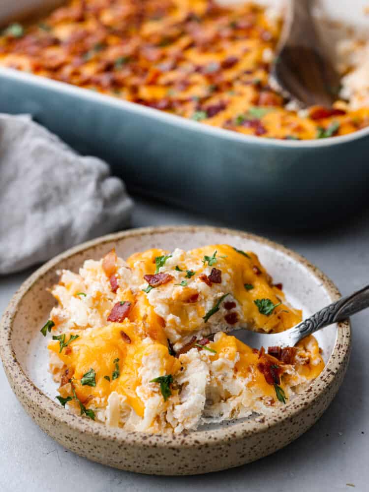 Just like the name says, these crack potatoes are so good you’ll be addicted! It’s an easy, cheesy side dish that the whole family will love. Shredded potatoes covered in a cheesy ranch sauce topped with bacon. What could be better? A scoop of potatoes served in a small, stoneware dish.