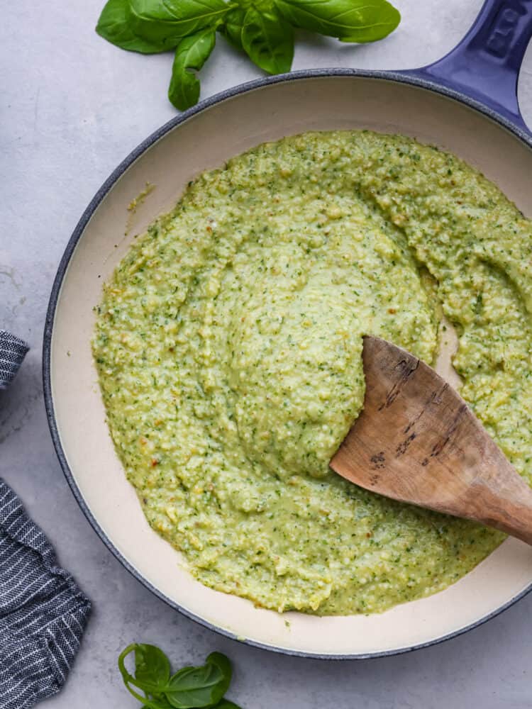 This creamy pesto sauce is so bright and packed with fresh flavor, and the best part is there is no cooking required! This quick and easy creamy sauce is ready in just 15 minutes and is perfect on your favorite cooked pasta. Creamy pesto in a sauce pan with a wooden spoon.