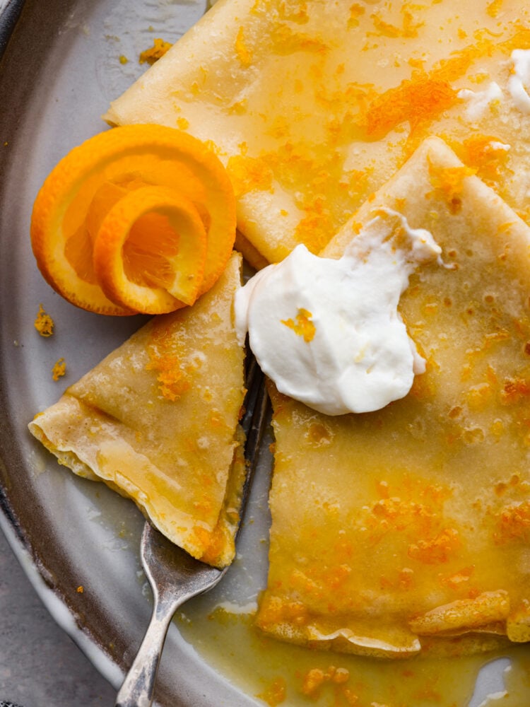 Light, airy, and bursting with juicy, orange flavor, these crepes suzette are the perfect dessert! Serve them on their own or with a scoop of vanilla ice cream on top for a French treat sure to make your stomach happy. Closeup of a bite being taken out of a crepe.