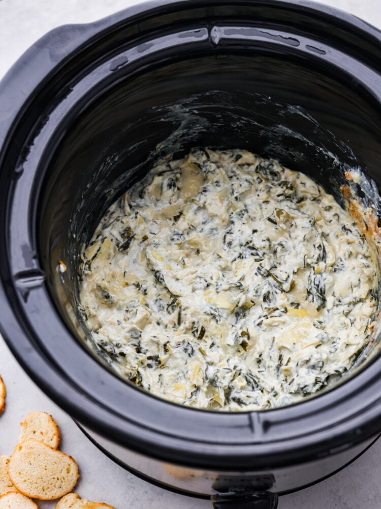 Crockpot spinach artichoke dip is the ultimate party pleaser! Not only is it delicious and creamy, but it's also super easy to make. Just toss all the ingredients in your crockpot and let it do its magic. Cooked spinach artichoke dip in the bottom of a crockpot.