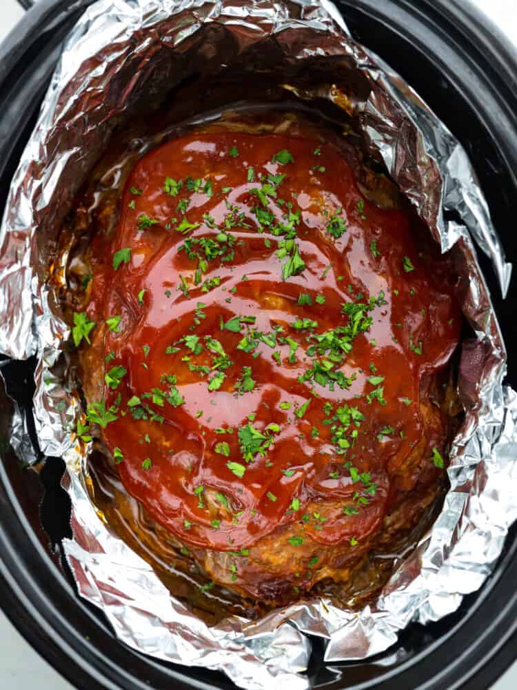 Meatloaf is a classic comfort food that is loved by the whole family! This recipe for crockpot meatloaf is easy to prepare, and using your slow cooker allows the flavors to blend together for a delicious meal. Top-down view of cooked meatloaf in a crockpot.