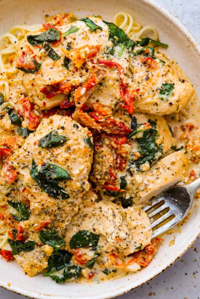 Crockpot Tuscan Chicken is delicious juicy and tender chicken breast cooked in a creamy parmesan and sun dried tomato sauce. It takes 10 minutes to prep and the smells alone will have your family asking when dinner is! Creamy crockpot Tuscan chicken on a plate with noodles.