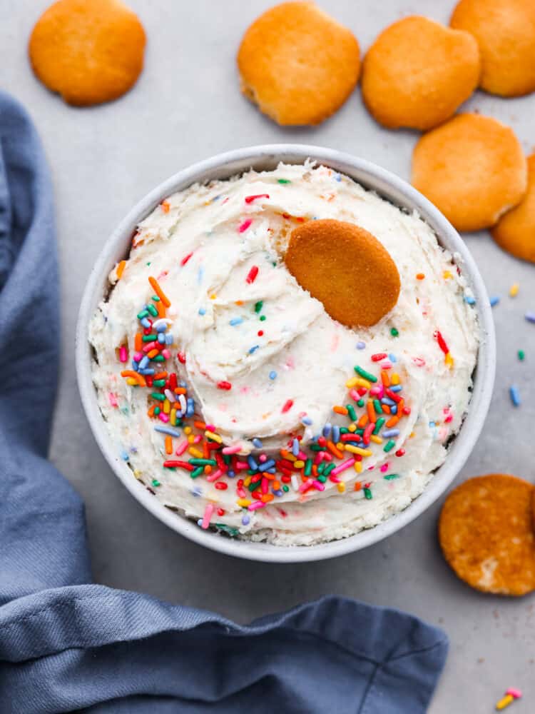 If you are looking for a quick and easy treat for a special occasion, this Dunkaroo Dip is your new go-to! It's a sweet dip perfect for cookies, apples, and graham crackers. It's colorful and absolutely addicting! An overhead view of dunkaroo dip with sprinkles and nilla wafers.