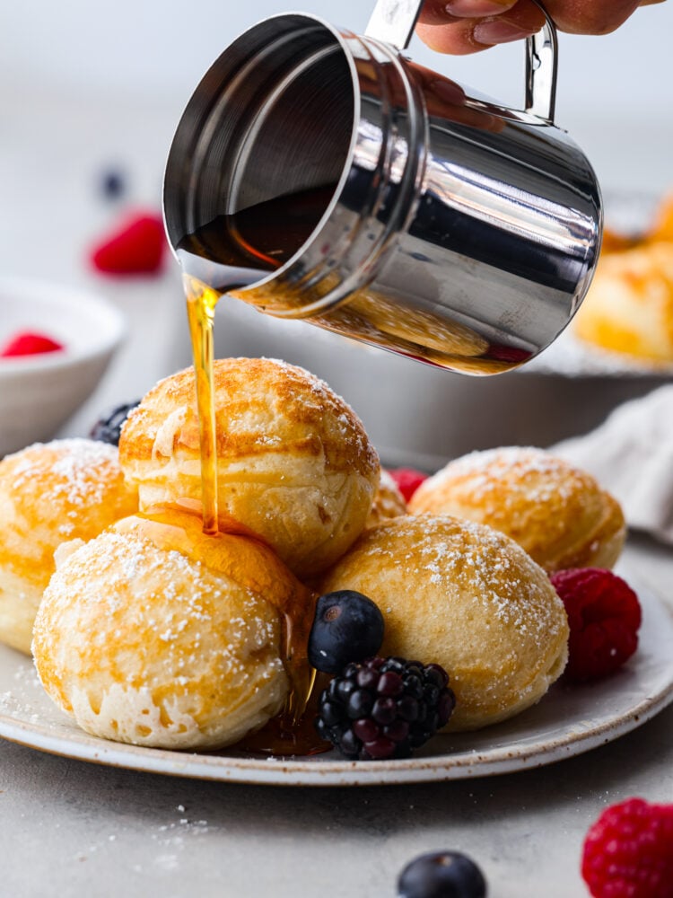 Ebelskivers are a Danish pancake that is cooked into a sphere using a special pan. They are fluffy and silky smooth on the inside, and you can fill them with anything from fresh berries to cream cheese. Flipping them in the pan is almost as fun as eating them! Ebelskivers on a plate with syrup being poured over them.