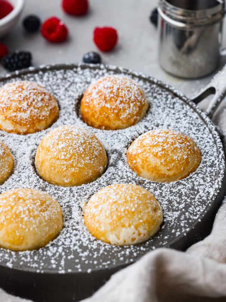 Ebelskivers are a Danish pancake that is cooked into a sphere using a special pan. They are fluffy and silky smooth on the inside, and you can fill them with anything from fresh berries to cream cheese. Flipping them in the pan is almost as fun as eating them! A side view of them in the pan with powdered sugar on top.