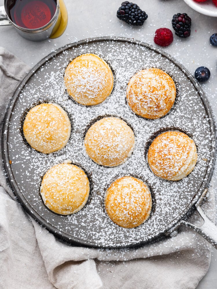 Ebelskivers are a Danish pancake that is cooked into a sphere using a special pan. They are fluffy and silky smooth on the inside, and you can fill them with anything from fresh berries to cream cheese. Flipping them in the pan is almost as fun as eating them! An overhead view of the ebelskivers cooked in their pan with powdered sugar on top.