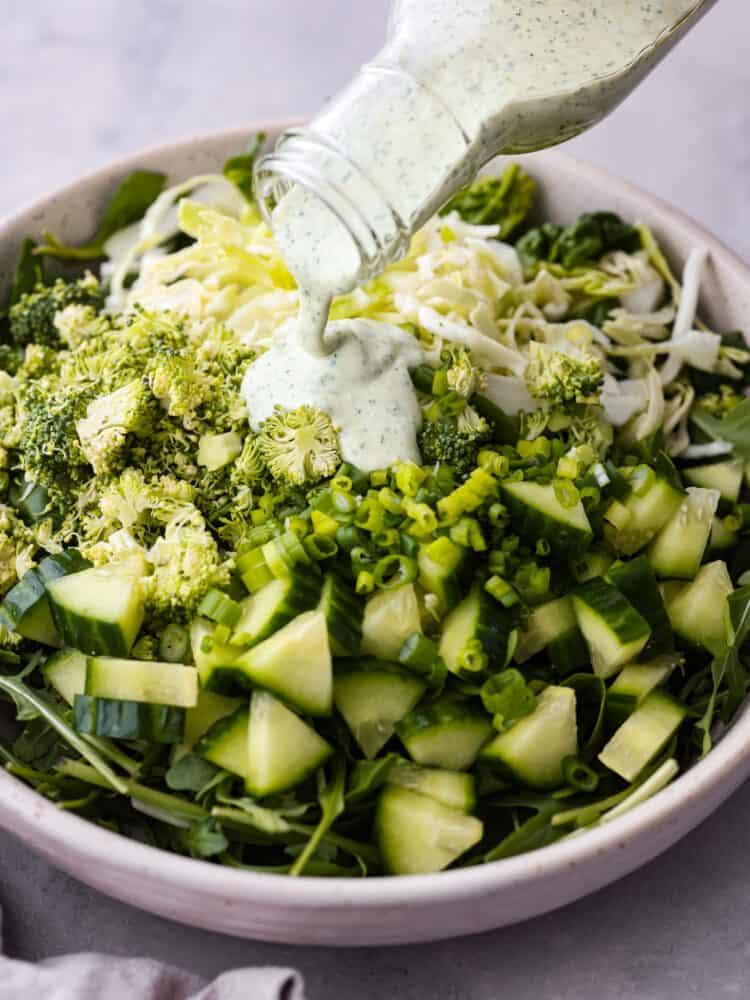 Meet your new favorite veggie fix- Green Goddess salad! Itโs packed with fresh lettuce, arugula, and spinach, tossed with green onions and the most flavorful Green Goddess dressing; creamy, savory goodness made with Greek yogurt, fresh herbs, and lemon! Salad dressing being poured over various greens.
