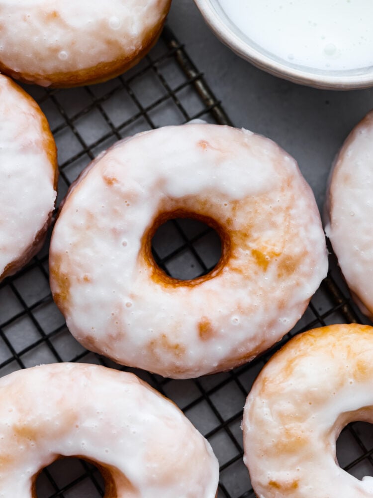 Homemade glazed donuts are light and fluffy with a perfectly moist inside and a sweetened glazed outside. They are the ultimate treat and super easy to make at home, which makes them the perfect dessert for any occasion. Seriously, who doesn't want a freshly fried homemade donut?! A close up on glazed donuts on a drying rack.