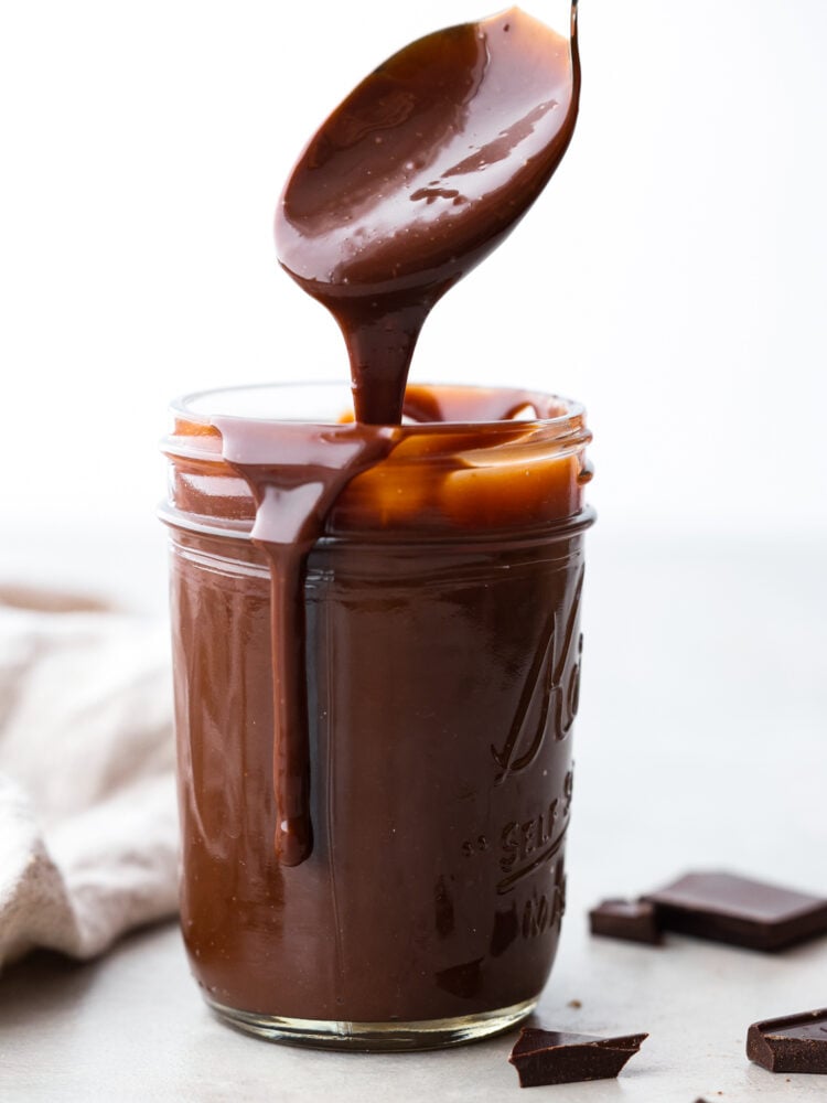 Homemade hot fudge is silky smooth and full of intense chocolate flavor without being too sweet. It is made up of 3 simple ingredients and ready in just 10 minutes. This is the perfect topping for hot fudge sundaes, fruit, and your favorite desserts! A spoon pulling out of a jar of hot fudge.