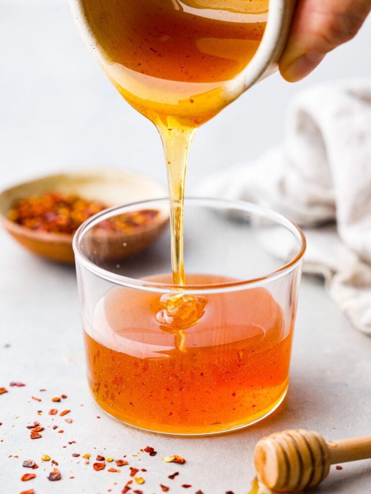 Get ready to meet your new favorite condiment! Hot honey is sweet but spicy and made by infusing honey with chili flakes and vinegar. It adds a kick of heat to anything from cornbread to fried chicken and is a fun way to spice up your favorite dishes. Hot honey being poured into a container.