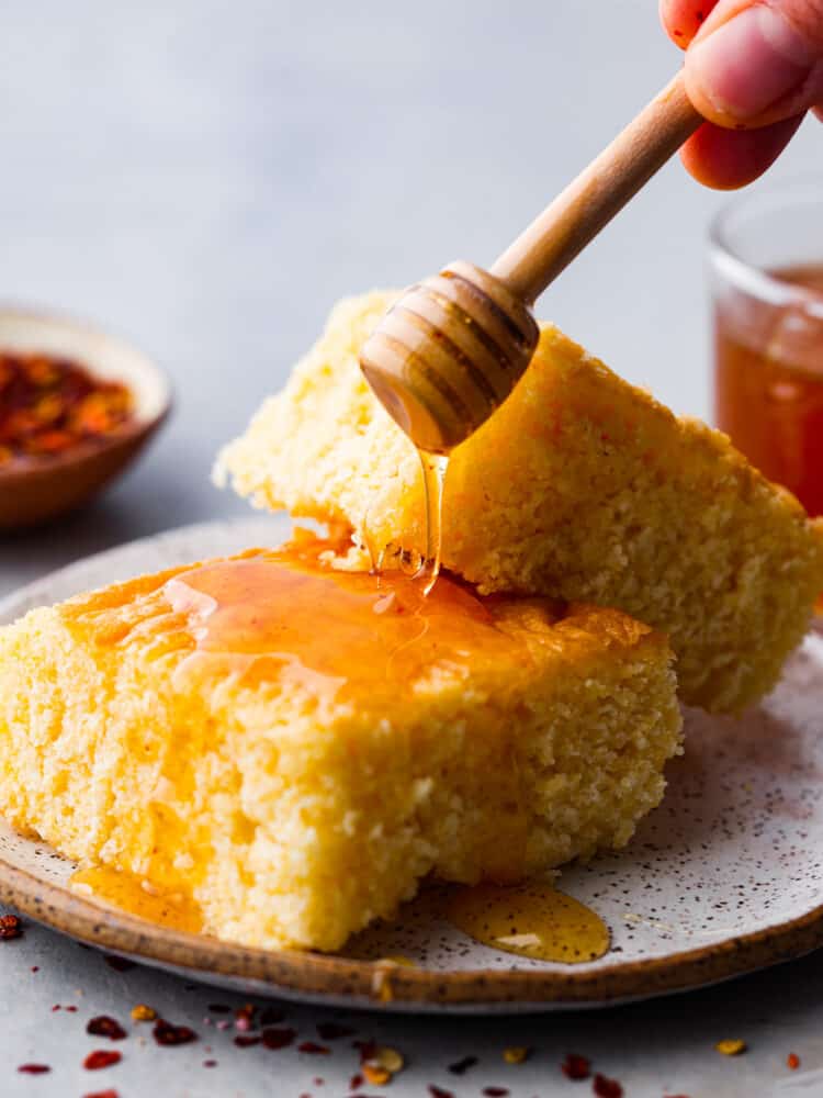 Get ready to meet your new favorite condiment! Hot honey is sweet but spicy and made by infusing honey with chili flakes and vinegar. It adds a kick of heat to anything from cornbread to fried chicken and is a fun way to spice up your favorite dishes. Drizzling honey over cornbread.