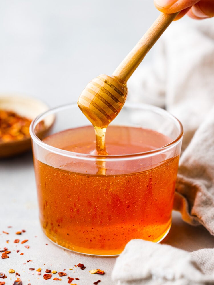 Get ready to meet your new favorite condiment! Hot honey is sweet but spicy and made by infusing honey with chili flakes and vinegar. It adds a kick of heat to anything from cornbread to fried chicken and is a fun way to spice up your favorite dishes. Hero image of hot honey served in a glass cup.