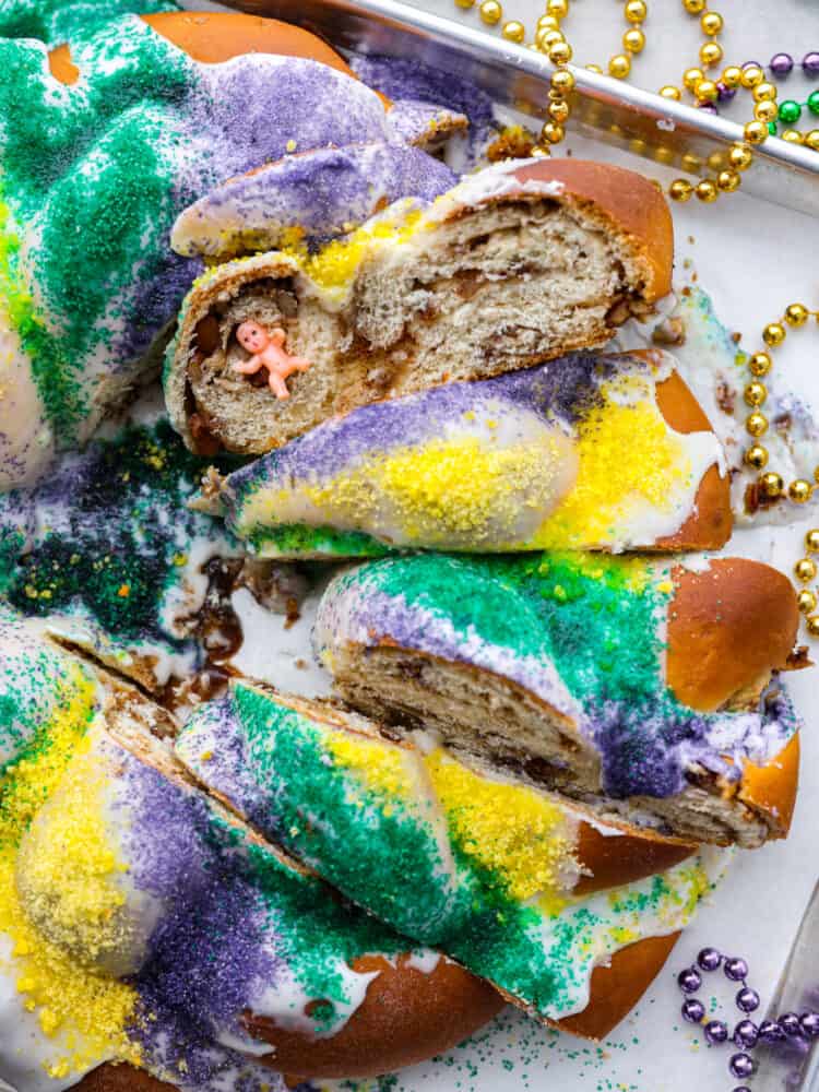King cake is a colorful and festive dessert for Mardi Gras celebrations! With its gorgeous swirl of purple, green and gold icing, this sweet and soft cake is a treat for both the eyes and the taste buds. Whether you're a seasoned king cake aficionado or a newcomer to this sugary delight, there's no denying its irresistible charm! King cake cut into slices.