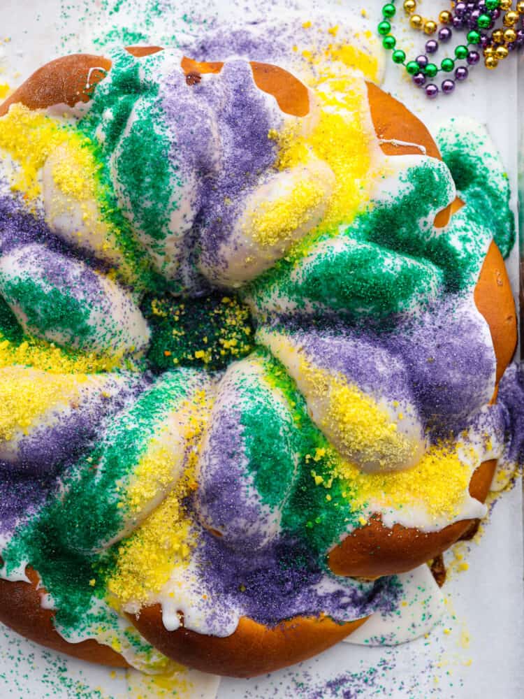 King cake is a colorful and festive dessert for Mardi Gras celebrations! With its gorgeous swirl of purple, green and gold icing, this sweet and soft cake is a treat for both the eyes and the taste buds. Whether you're a seasoned king cake aficionado or a newcomer to this sugary delight, there's no denying its irresistible charm! Top-down view of king cake, covered in purple, yellow, and green sanding sugar.