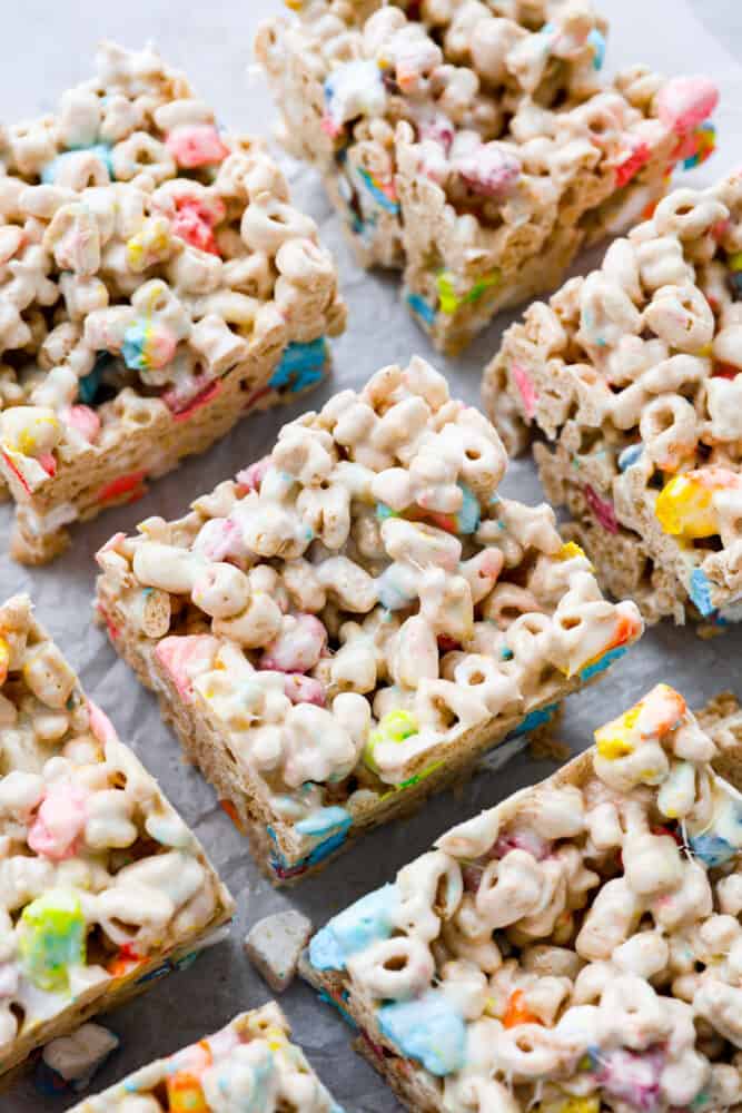 These Lucky Charms treats are a fun twist on the classic rice krispie treat and are every bit as magically delicious as you could imagine! They are sweet, but not too sweet to keep coming back for seconds and even thirds. They are a colorful and quick treat perfect for every occasion. Lucky charms treats cut into bars on top of parchment paper.