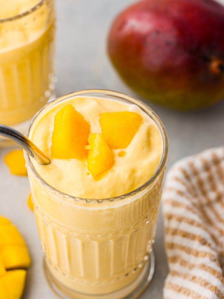 This Mango Lassi is an Indian yogurt smoothie that is so creamy and full of flavor. It's spiced with cardamom to give it a little kick, and it will have you coming back for seconds. It will be an instant hit every time you serve it! A top view of a mango lassi with a few chunks of mango on top.