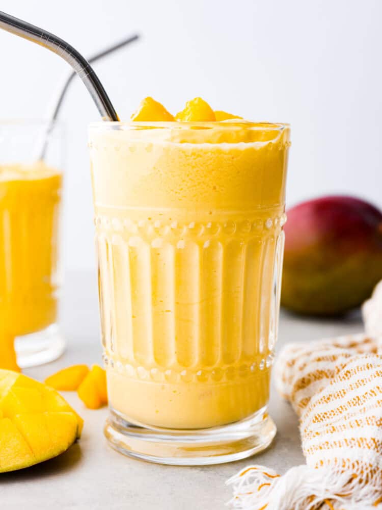 This Mango Lassi is an Indian yogurt smoothie that is so creamy and full of flavor. It's spiced with cardamom to give it a little kick, and it will have you coming back for seconds. It will be an instant hit every time you serve it! A mango lassi in a glass cup with a metal straw.