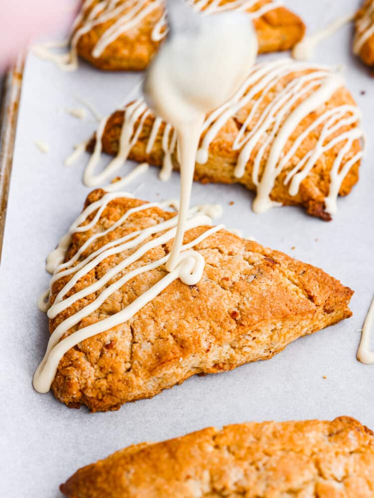 Golden and flaky Maple Pecan Scones are buttery soft and full of nutty flavor from toasted pecans and real maple syrup. They are melt in your mouth delicious and ridiculously easy to make! A spoon drizzling maple glaze over the top of the scone.
