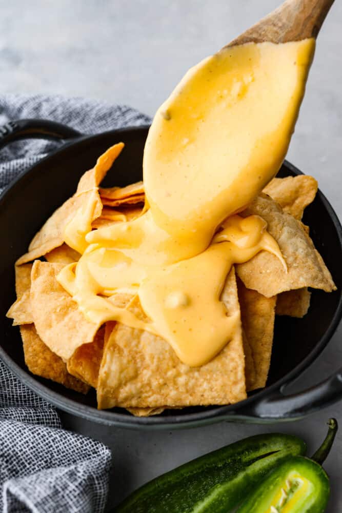 This Nacho Cheese recipe is the genuine Velveeta based topping that is full of nostalgia and amazing flavor! It's so simple to whip up and tastes way better than store-bought. Nacho cheese being poured over tortillas.