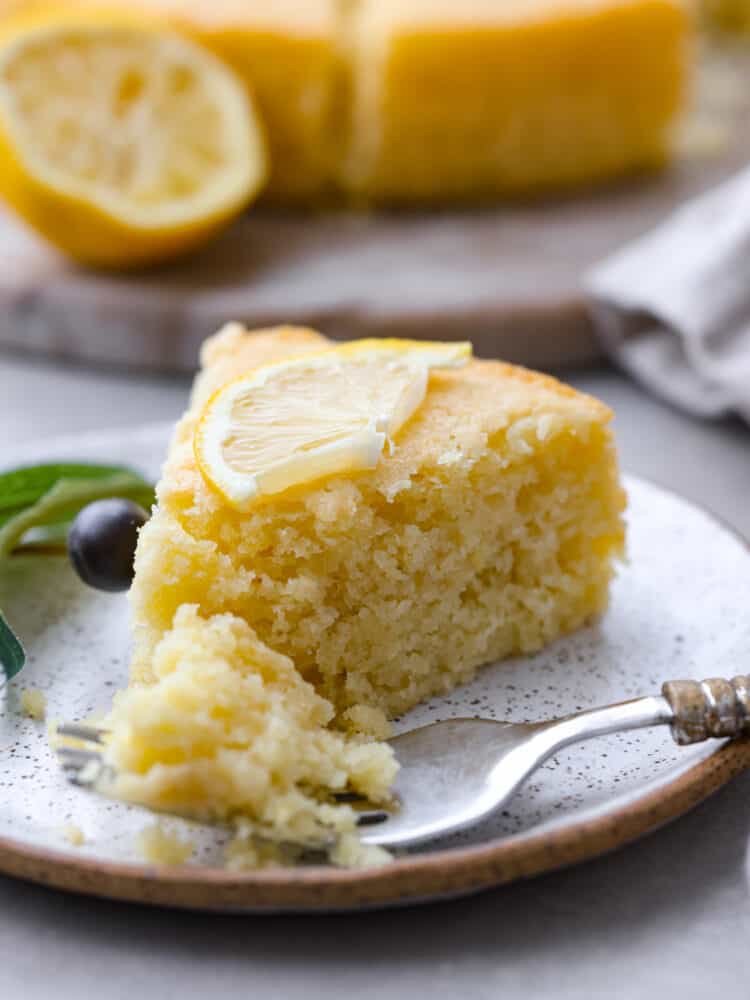 If youโve never tried it, (which you definitely should!) olive oil cake has a light and moist texture, with a slightly crispy crust. The flavor is delicate and subtle, with fruity and nutty notes. You will love every bite! A slice of cake on a stoneware plate.