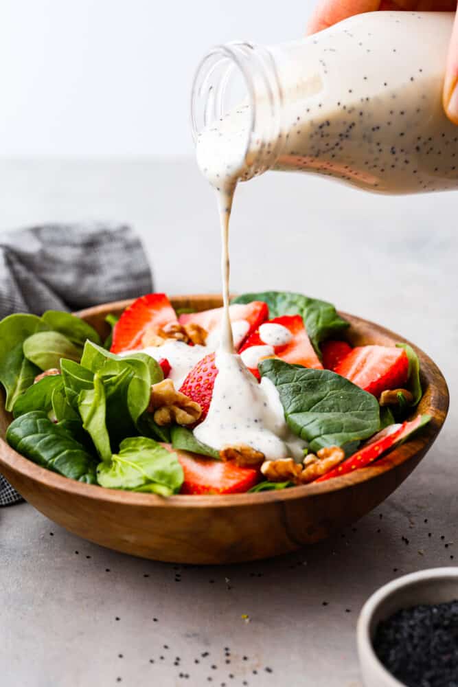 Creamy poppyseed dressing is creamy, sweet, and a little tangy. With just 5 simple ingredients, it's perfect on top of a fresh green salad and is a must-have in your recipe book! Creamy poppyseed dressing being poured over the top of a fresh salad.