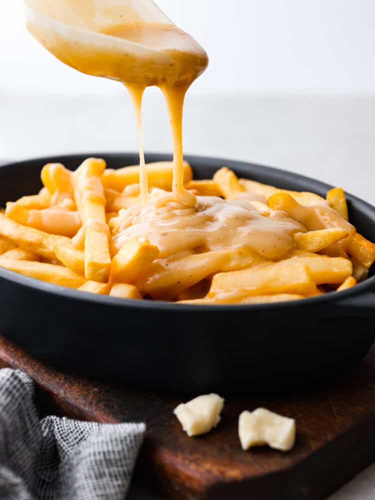 Poutine is a famous Canadian dish that you are going to love making at home! Delicious crispy fries topped with savory gravy and cheese curds are exactly what every party needs. You can serve them as an appetizer or side for any occasion! French fries in a dish with gravy being poured over them.