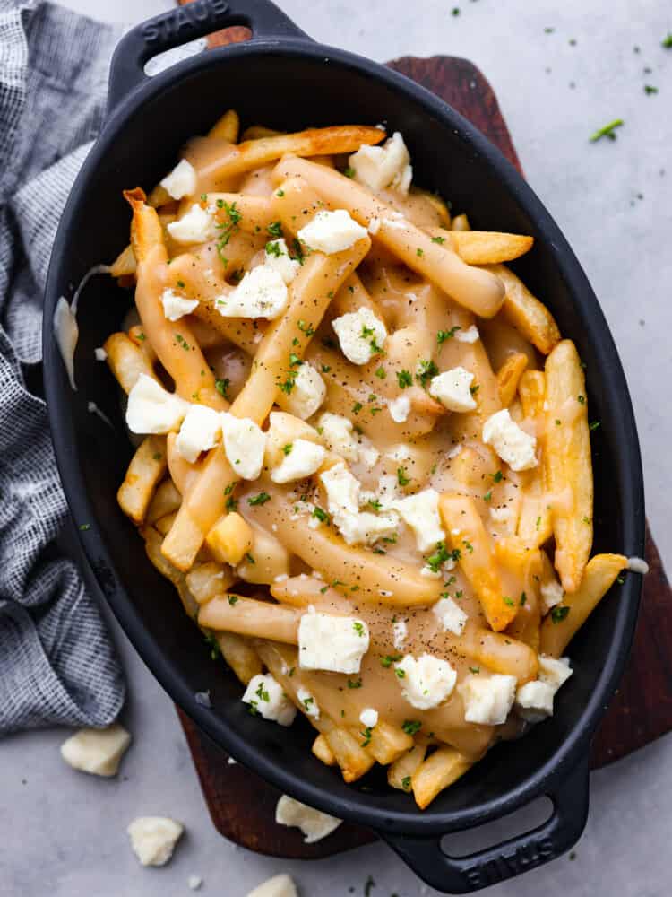 Poutine is a famous Canadian dish that you are going to love making at home! Delicious crispy fries topped with savory gravy and cheese curds are exactly what every party needs. You can serve them as an appetizer or side for any occasion! Poutine in a black dish.