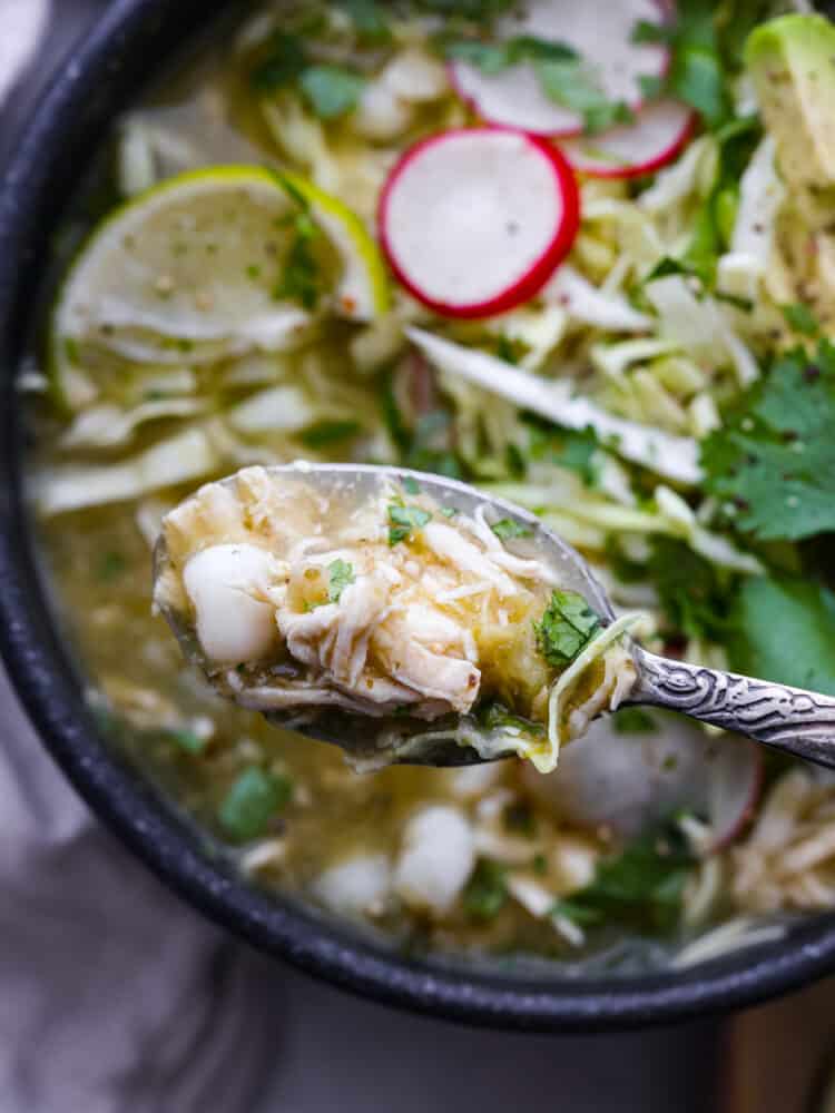 Pozole verde is a flavorful Mexican soup with fresh verde and shredded chicken. It is topped with ingredients like shredded cabbage, radishes, and lime for a bright, fresh, and flavor packed dish. It is the perfect soup for any occasion! A close up on the pozole on a spoon.