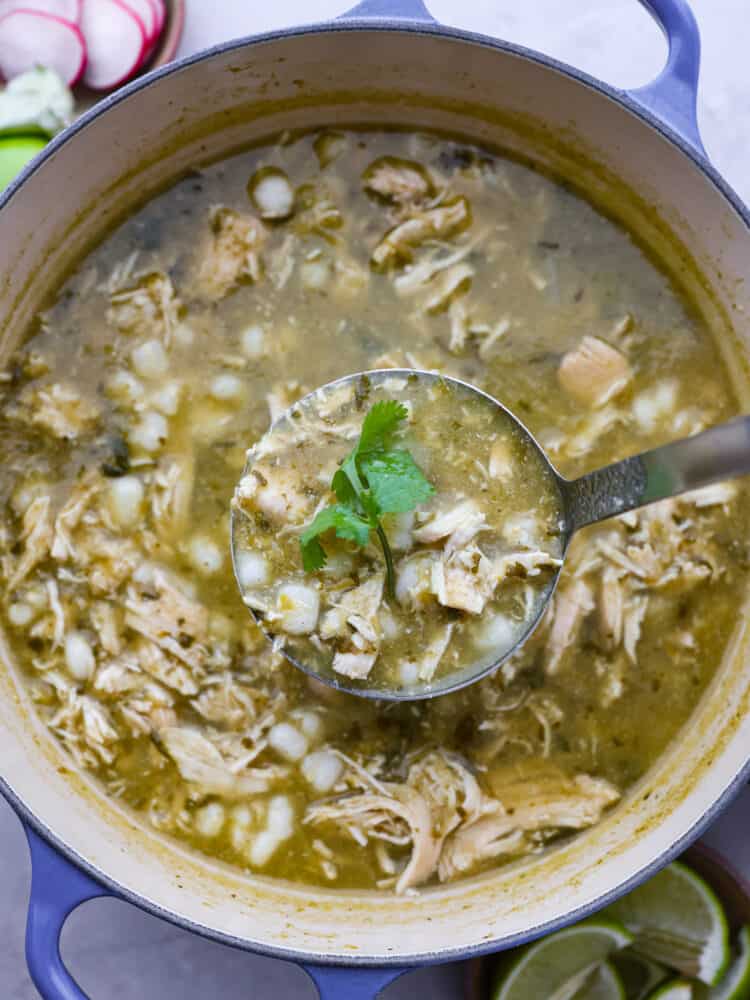 Pozole verde is a flavorful Mexican soup with fresh verde and shredded chicken. It is topped with ingredients like shredded cabbage, radishes, and lime for a bright, fresh, and flavor packed dish. It is the perfect soup for any occasion! The pozole in a pot with a ladle taking a spoonful out.