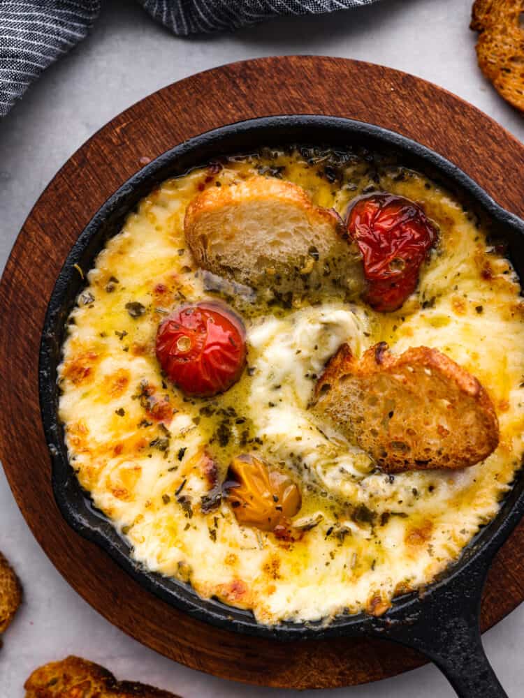 Provoleta is a traditional Argentine dish made from melted provolone cheese served in a hot skillet. It has a gooey, melted texture with a rich and salty flavor that is perfect for dipping with crusty bread. I've added pesto and tomatoes for an extra pop of bubbling flavor. This is one dip you don't want to miss! Top-down view of provoleta in a small skillet.
