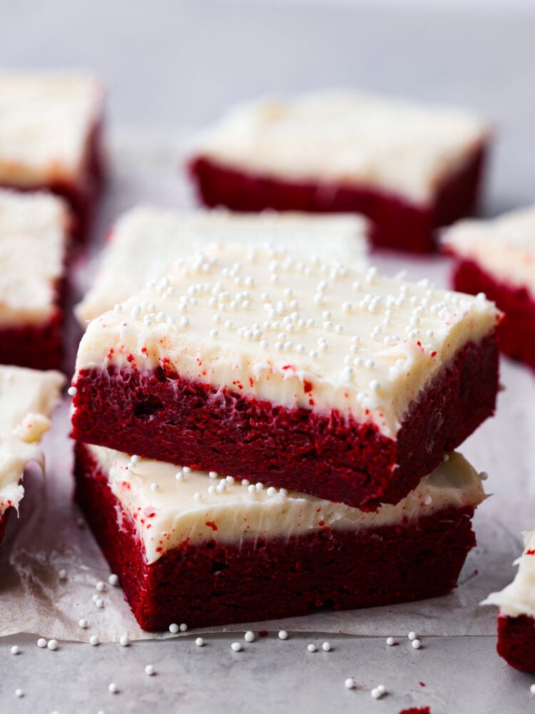 These decadent red velvet sugar cookie bars with cream cheese frosting are so divine. This is the best of both worlds, all the goodness of red velvet cake in an easy-to-make cookie bar form. Hero image of 2 cookie bars stacked on top of each other.