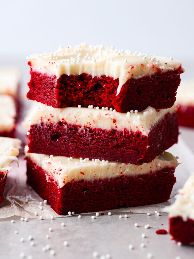 These decadent red velvet sugar cookie bars with cream cheese frosting are so divine. This is the best of both worlds, all the goodness of red velvet cake in an easy-to-make cookie bar form. 3 cookie bars stacked on top of each other.
