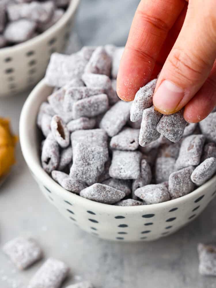 If you crave a peanut butter and chocolate snack with less calories, these Skinny Muddy Buddies are your new best friend! They taste just as good as the muddy buddies you remember, without the guilt. A hand grabbing the chex mix snack out of the white and black bowl
