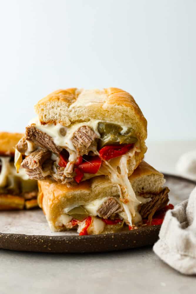 You'll never want to make a Philly cheesesteak any other way! Slow Cooker Philly Cheesesteaks are juicy and tender meat cooked in the slow cooker and perfectly topped with melty cheese on a toasted bun! Slow cooker philly cheesesteak sandwiches stacked on top of each other.
