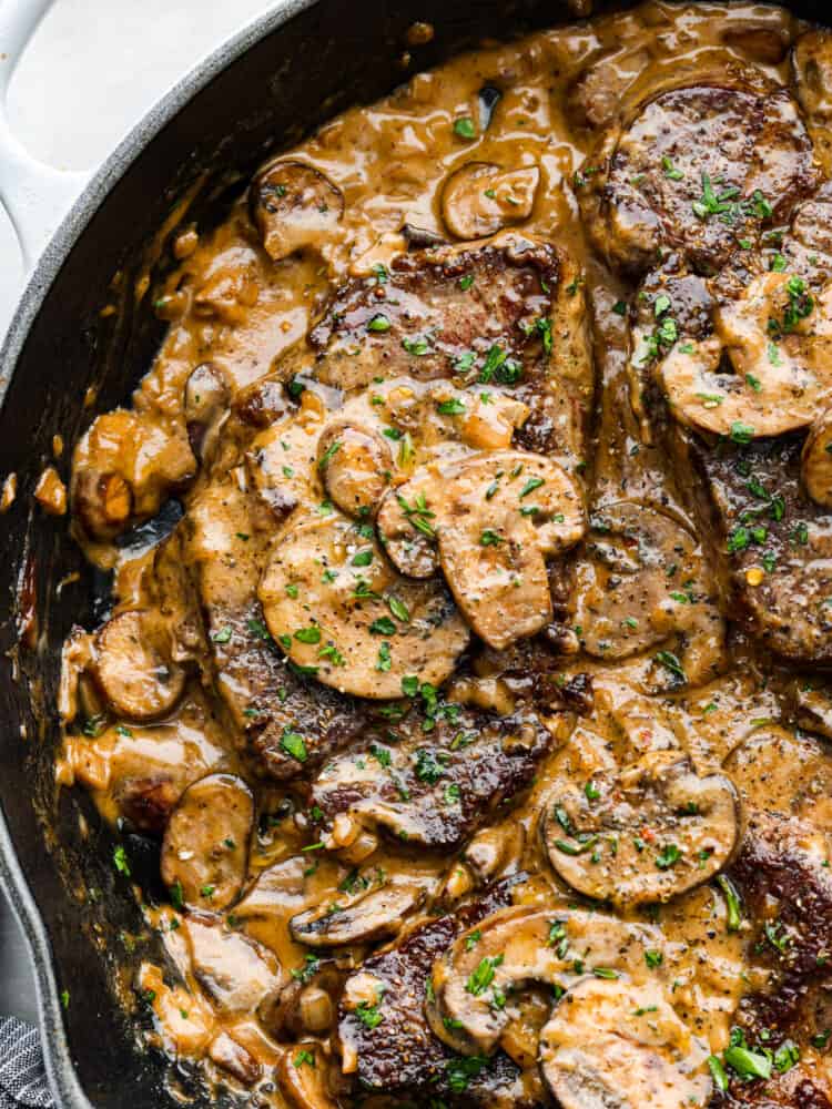 Juicy and succulent Steak Diane is the perfect dinner for any occasion. Diane refers to the delicious cream sauce made that includes mustard, Worcestershire sauce, and Cognac. The steak is flattened and seared in butter, and couldn't be more flavorful! A close up of all the mushrooms and steak in a black skillet