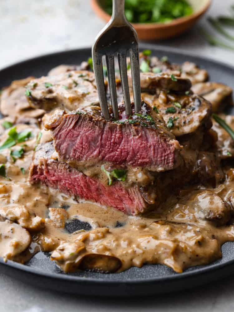 Juicy and succulent Steak Diane is the perfect dinner for any occasion. Diane refers to the delicious cream sauce made that includes mustard, Worcestershire sauce, and Cognac. The steak is flattened and seared in butter, and couldn't be more flavorful! A fork grabbing a piece of food.