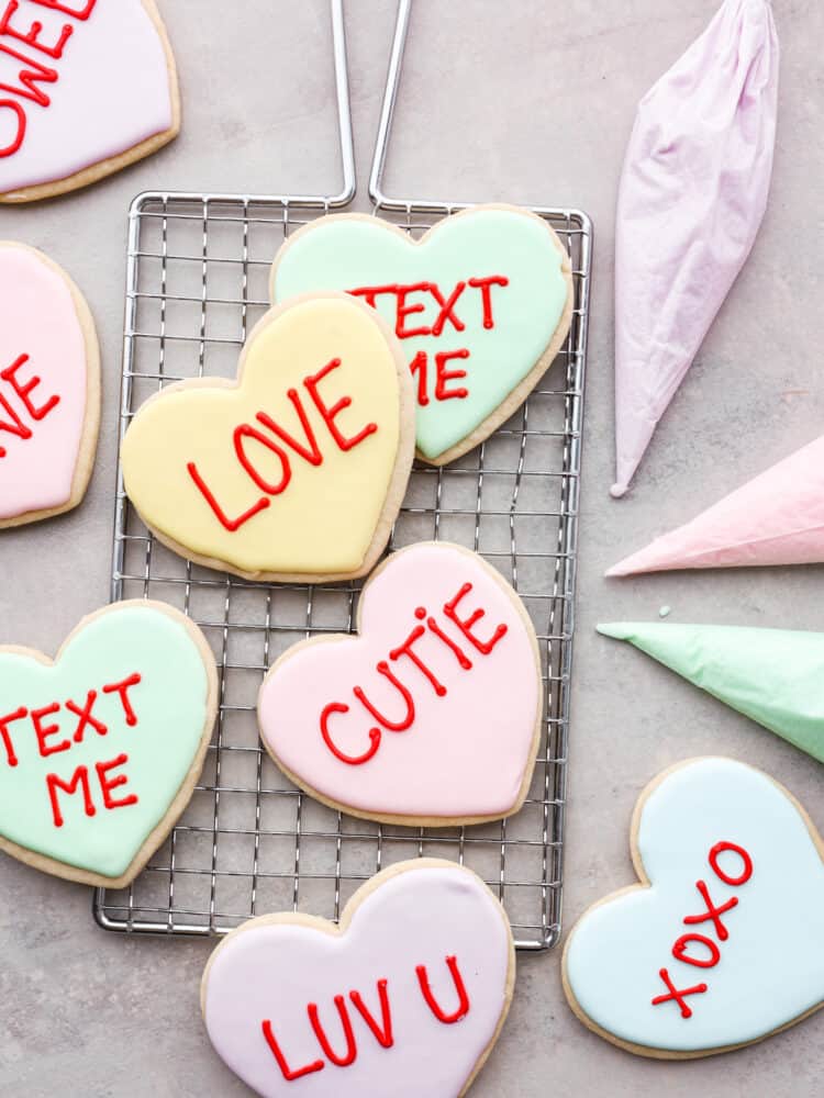 Show your sweetheart how much you care with these adorable Valentine's Day cookies! Conversation heart cookies are fun and nostalgic and are customizable with sweet and silly messages. They are delicious, easy to make, and totally unforgettable! Valentine's day cookies on a cooling rack with fun sayings on them like "text me" and "cutie".