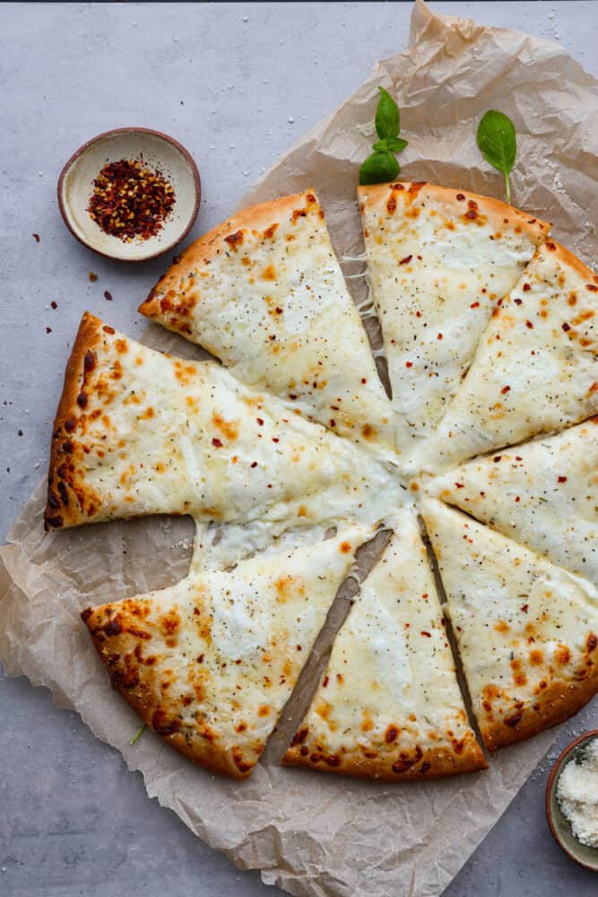 White Pizza, also called pizza bianca, is a delicious and soft and chewy pizza crust topped with a creamy Parmesan sauce and mozzarella cheese. There's every reason to fall in love with this recipe. It's quick and easy and a total hit! White pizza all sliced up on top of parchment paper.