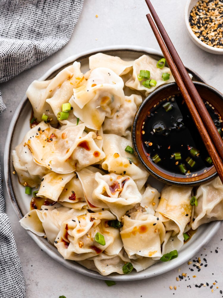 Skip the takeout and make these irresistible pork wontons at home! Theyโre soft and juicy and filled with mouthwatering seasoned pork. You wonโt be able to stop at one! Top-down view of boiled wontons served on a white plate with soy sauce.