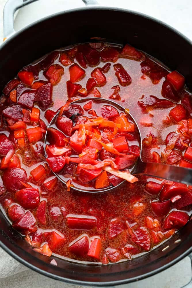 Borscht: the perfect soup for when you want to feel healthy but need something packed with flavor. It's like a hug in a bowl, if that hug was made of beets and potatoes. This tasty Ukrainian soup will become a new family favorite! Top-down view of borscht being scooped up with a ladle in a large pot.