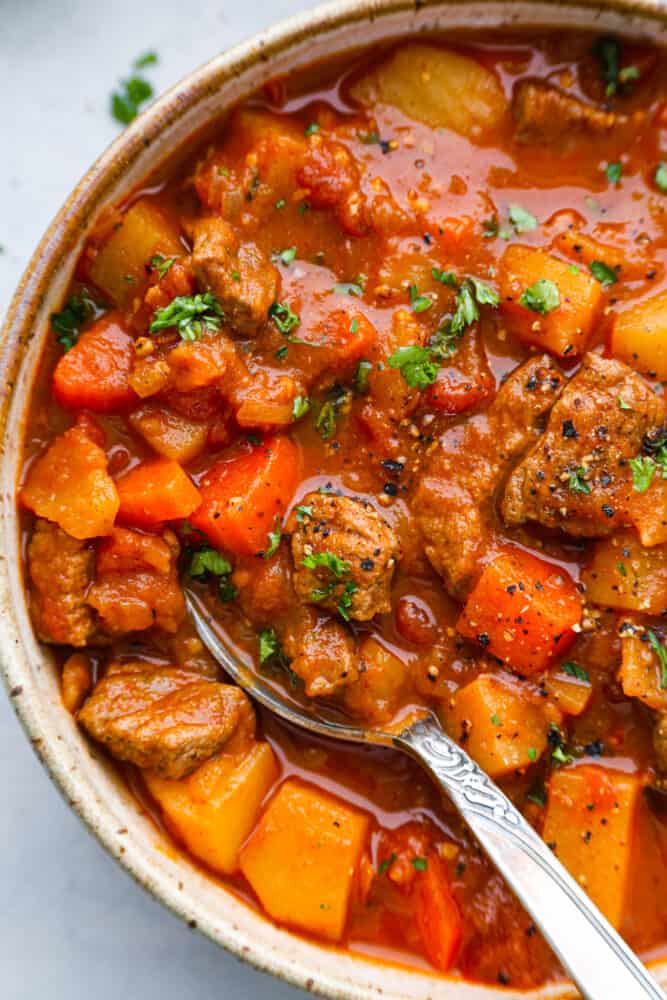 Hungarian goulash is a hearty and scrumptious beef stew that is Hungary's national dish. Beef is slow-cooked with onions, tomatoes, carrots, and potatoes to make this the ultimate comfort food and perfect dish for cold days. A close up on Hungarian goulash in a bowl with a spoon.