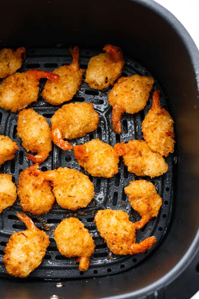 Seafood lovers! Here is the EASIEST way to make crispy, breaded shrimp in the air fryer! Making air fryer frozen shrimp takes less than 10 minutes and turns out perfectly every time. The hardest part is choosing what dipping sauce to serve it with! Cooked shrimp in the bottom of an air fryer basket.