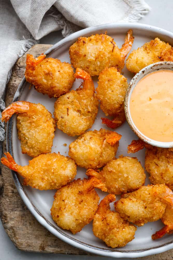 Seafood lovers! Here is the EASIEST way to make crispy, breaded shrimp in the air fryer! Making air fryer frozen shrimp takes less than 10 minutes and turns out perfectly every time. The hardest part is choosing what dipping sauce to serve it with! Cooked, breaded shrimp served on a gray plate.
