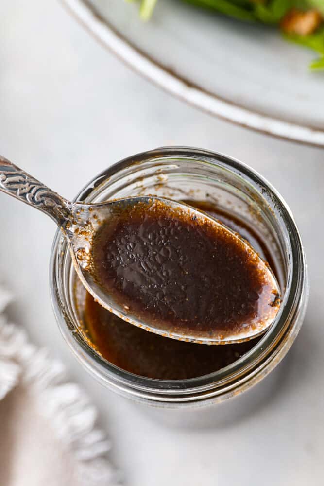 Balsamic Vinaigrette is a staple in the kitchen that every cook should have the perfect recipe for. THIS is that perfect recipe! It's tangy and refreshing, and will spruce up your salads and better than every other recipe I've ever tried. A close up on the balsamic vinaigrette on a spoon over a mason jar.