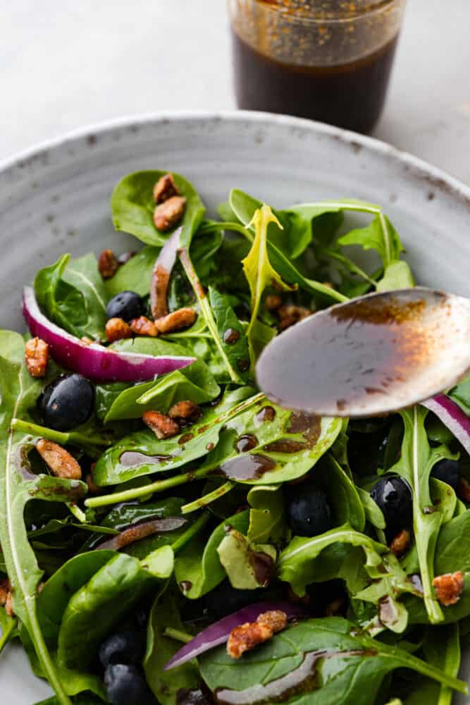 Balsamic Vinaigrette is a staple in the kitchen that every cook should have the perfect recipe for. THIS is that perfect recipe! It's tangy and refreshing, and will spruce up your salads and better than every other recipe I've ever tried. A spoon pouring the dressing over a salad.