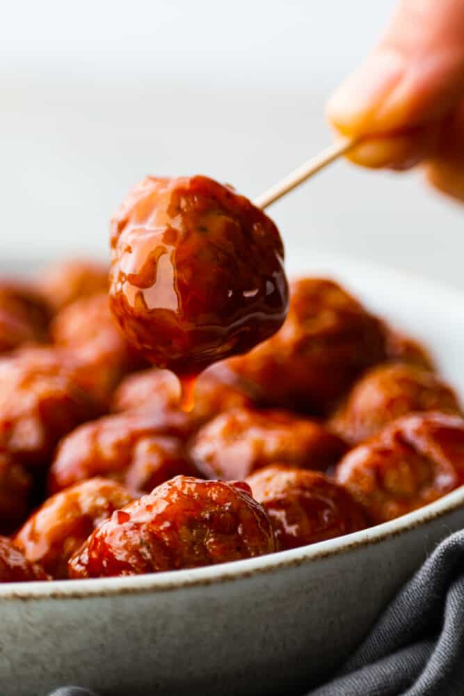 BBQ Meatballs are cooked in a slow cooker and smothered in a delicious barbecue sauce. They are the easiest meatball recipe you'll ever try, and they are perfect for parties and simple appetizers. A bbq meatball on a toothpick.