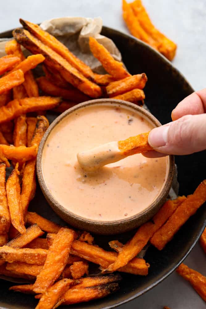 Boom Boom Sauce is a sweet and spicy mayonnaise-based sauce that is perfect for dipping! It takes 5 minutes to whip up and is so full of flavor, making it perfect for fries, onion rings, and so much more. A hand dipping a french fry into the boom boom sauce.
