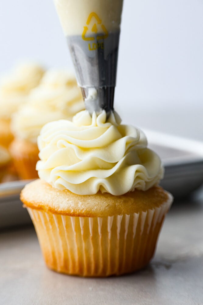 A cupcake being frosted with buttercream frosting. 